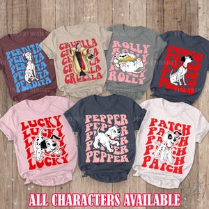 May include: Six different t-shirts featuring characters from the Disney film 101 Dalmatians. The shirts are in various colours, including brown, beige, grey, pink, and white. Each shirt features a different character, including Cruella De Vil, Rolly,  Lucky, Pepper, Patch, and Perdita. The shirts all have the character's name repeated in a retro font.