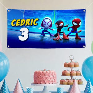 May include: A blue banner with the name "Cedric" and the number "3" in yellow and white, featuring cartoon characters. The banner is decorated with images of Spider-Man characters. Party decorations include a pink cake, cupcakes, and balloons.