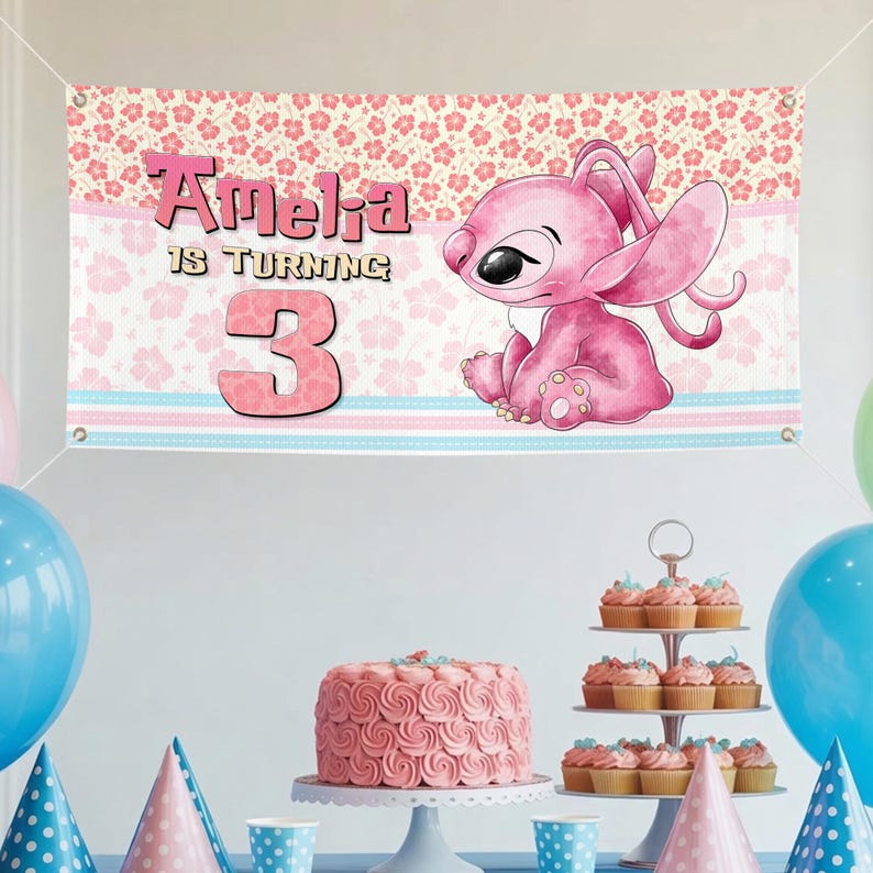 May include: A pink banner with the text "Amelia is turning 3" and a cartoon character. The banner has a floral pattern at the top and blue and pink stripes at the bottom. The banner is displayed at a birthday party with a cake and cupcakes.