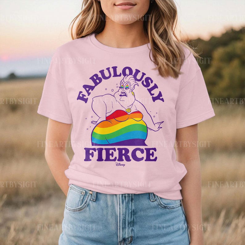 Peut inclure: T-shirt rose clair avec une illustration de la m&eacute;chante Ursula de La Petite Sir&egrave;ne. Le design comprend les mots "FABULOUSLY FIERCE" en violet, et le corps d'Ursula est un arc-en-ciel.