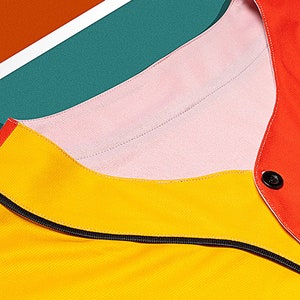 May include: Close-up of a yellow, pink, and red collared shirt with a black zipper. The shirt has a button on the right side of the collar.