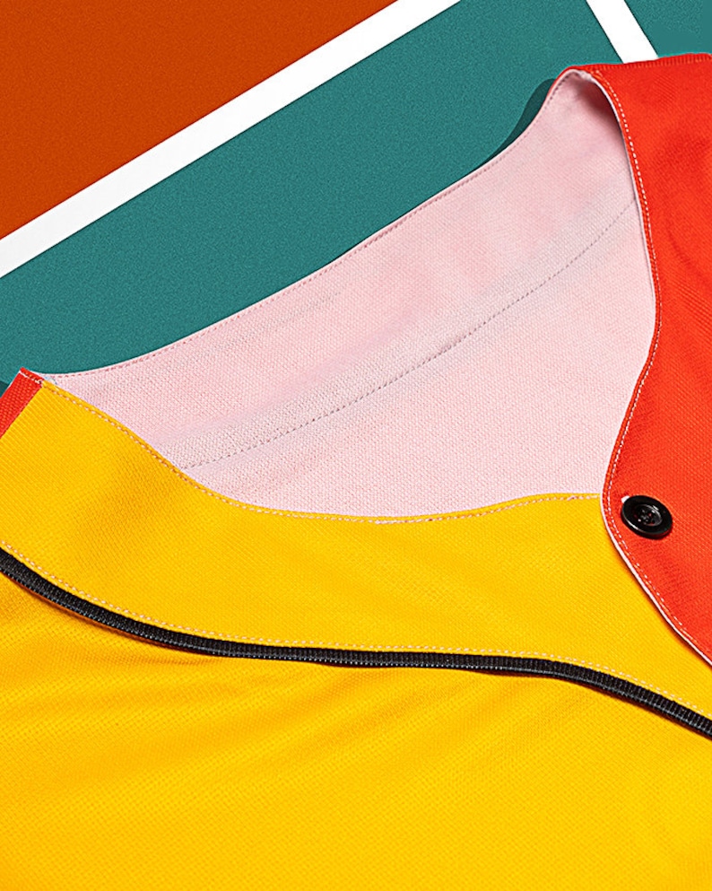 May include: Close-up of a yellow, pink, and red collared shirt with a black zipper. The shirt has a button on the right side of the collar.