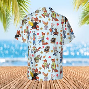 May include: A light blue short-sleeve button-down shirt featuring an all-over repeating pattern of cartoon characters from Zootopia, including foxes, rabbits, and other animals, interspersed with small orange carrot and yellow badge icons.