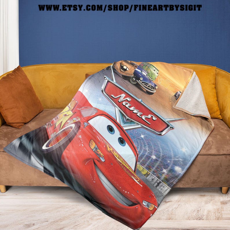 May include: A plush blanket featuring Lightning McQueen from the Cars movie. The red race car is prominently displayed, along with other characters and the word "Name" on a red emblem. The blanket is draped over a gold sofa.