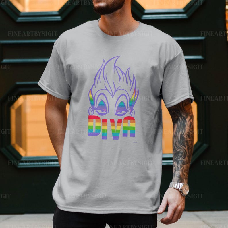 Op de afbeelding: Een grijs T-shirt met het gezicht van een cartoonfiguur en het woord "DIVA" in regenboogkleuren.