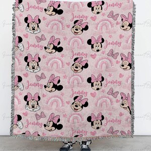 K&ouml;nnte beinhalten: Rosa gewebte Decke mit Minnie Mouse-Gesichtern, Schleifen, Regenbogen und Herzen. Der Name "Jenny" ist wiederholt im Design enthalten. Die Decke hat einen Fransenrand und ist f&uuml;r ein Kinderzimmer geeignet.