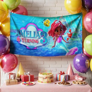 May include: A birthday party scene with a banner featuring a mermaid illustration and the text "AMELIA IS TURNING 3." The banner is surrounded by balloons, gifts, a cake, and party hats. The mermaid has red hair and a blue tail.