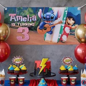 May include: A party scene with a banner saying "Amelia is turning 3." The banner shows cartoon characters Stitch playing a guitar and Lilo with a surfboard. A red and black cake with a yellow lightning bolt sits on a table with cupcakes and superhero-themed cups.