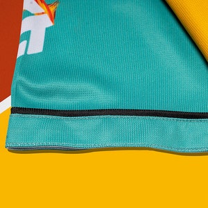 May include: Close-up of a teal blue fabric with a black trim. The fabric has a subtle texture and is folded over on itself.