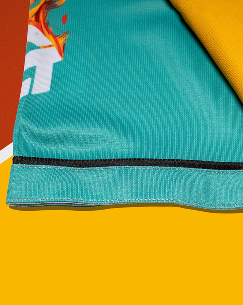 May include: Close-up of a teal blue fabric with a black trim. The fabric has a subtle texture and is folded over on itself.