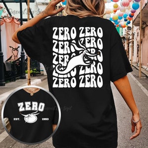 Puede incluir: Camiseta negra con un gr&aacute;fico blanco de Zero de Pesadilla Antes de Navidad. El gr&aacute;fico presenta la cara y el cuerpo de Zero con el texto "ZERO ZERO" repetido en un estilo retro. La parte posterior de la camiseta tiene el texto "ZERO" con una imagen estilizada de la cabeza de Zero y el texto "EST. 1993".