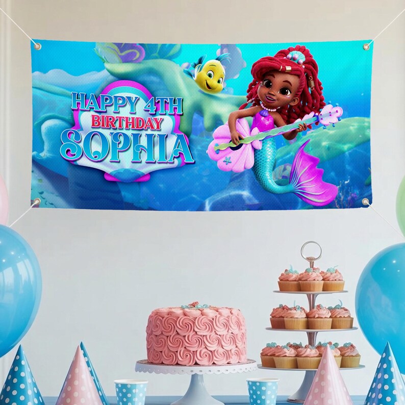 K&ouml;nnte beinhalten: Ein blaues Banner mit dem Text "HAPPY 4TH BIRTHDAY SOPHIA" und einer Cartoon-Meerjungfrau, die ein Musikinstrument spielt. Das Banner zeigt eine Unterwasserszene. Ein rosa Kuchen und Cupcakes stehen auf einem Tisch mit Luftballons.