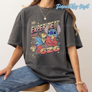 May include: A dark gray t-shirt with a vintage-style graphic of Stitch from Lilo & Stitch. The graphic features Stitch in a red spacesuit with the text "Experiment 626" and "Stitch" above it.