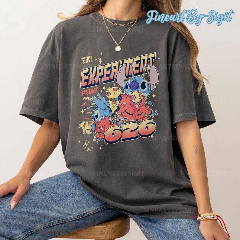 May include: A dark gray t-shirt with a vintage-style graphic of Stitch from Lilo & Stitch. The graphic features Stitch in a red spacesuit with the text "Experiment 626" and "Stitch" above it.