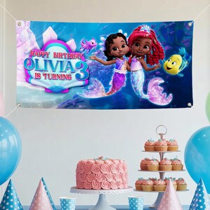 Peut inclure: Banni&egrave;re bleue avec l'inscription "HAPPY BIRTHDAY OLIVIA 3 IS TURNING", repr&eacute;sentant deux sir&egrave;nes et un poisson jaune. La banni&egrave;re a un fond sur le th&egrave;me de la mer. Id&eacute;ale pour une f&ecirc;te d'anniversaire.