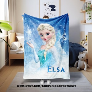 Puede incluir: Una manta azul y blanca con Elsa de Frozen. La imagen muestra a Elsa con cabello rubio y un vestido azul, sobre un fondo nevado. El nombre "Elsa" est&aacute; impreso en azul. La URL de la tienda de Etsy es visible en la parte inferior.