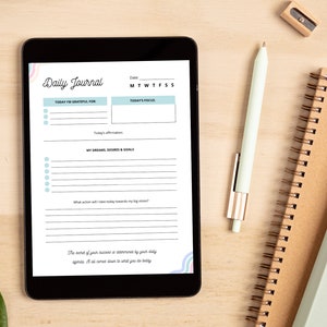 Pode incluir: Um tablet digital exibindo um modelo de di&aacute;rio di&aacute;rio com se&ccedil;&otilde;es para gratid&atilde;o, foco, sonhos e objetivos. O tablet est&aacute; em uma superf&iacute;cie de madeira com uma caneta, um l&aacute;pis e um caderno.