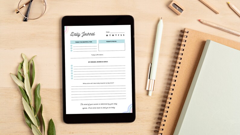 Pode incluir: Um tablet digital exibindo um modelo de di&aacute;rio di&aacute;rio com se&ccedil;&otilde;es para gratid&atilde;o, foco, sonhos e objetivos. O tablet est&aacute; em uma superf&iacute;cie de madeira com uma caneta, um l&aacute;pis e um caderno.