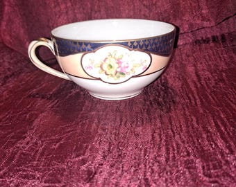 May include: A white teacup with a pink and gold floral design and a blue and gold geometric pattern around the rim.