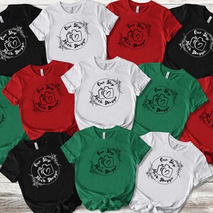 Pode incluir: Dez camisetas diferentes em várias cores, cada uma com um design gráfico preto e branco de uma câmera com o texto "One Stop Shoppe" e um coração.