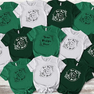 Puede incluir: Diez camisetas en varios tonos de verde y blanco con un diseño gráfico en blanco y negro que presenta una cámara con un corazón en su interior y el texto "One Step Mock Shoppe". Una camiseta tiene el texto "Your Design Here" en un círculo.