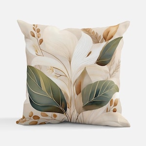 May include: Square decorative pillow with a botanical design. The pillow features a watercolor illustration of large green leaves, cream-colored flowers, and brown accents on a beige background. The pillow has a soft, inviting appearance.