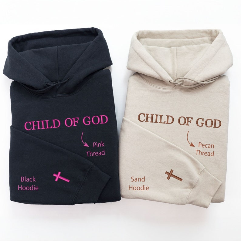 Op de afbeelding: Twee hoodies, een zwarte en een zandkleurige, met de tekst "CHILD OF GOD" geborduurd op de voorkant. De zwarte hoodie heeft roze draad en de zandkleurige hoodie heeft pecannotendraad. Beide hoodies hebben een kruis geborduurd op de mouw.