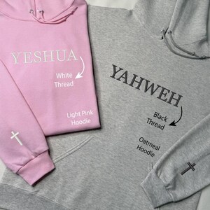 May include: Two hoodies, one light pink and one oatmeal. The light pink hoodie has "YESHUA" printed in white thread. The oatmeal hoodie has "YAHWEH" printed in black thread. Both hoodies have a cross on the sleeve.