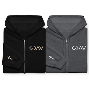 May include: Two zip-up hoodies, one black and one dark gray, each featuring a white G>AV symbol on the left chest and a small white cross graphic on the right sleeve. Both garments include a hood, a full-length front zipper, and long sleeves.