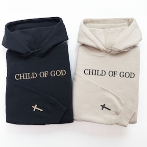 Op de afbeelding: Twee hoodies, een zwarte en een beige, met de tekst "CHILD OF GOD" op de voorkant en een kruis op de mouw.