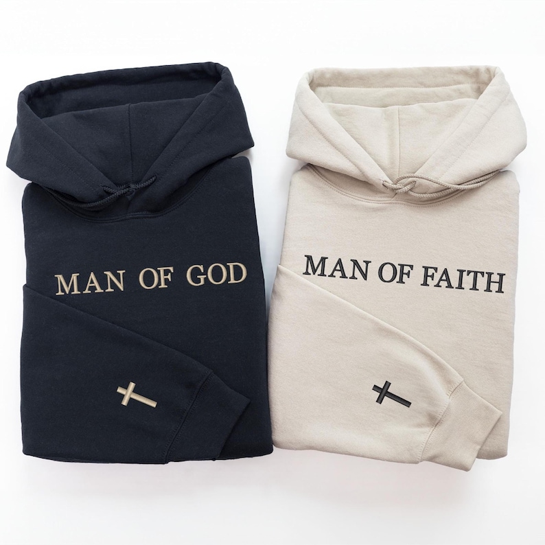 Peut inclure: Deux sweats &agrave; capuche pli&eacute;s, un noir et un beige. Le sweat &agrave; capuche noir porte l'inscription "MAN OF GOD" brod&eacute;e sur le devant et une croix sur la manche. Le sweat &agrave; capuche beige porte l'inscription "MAN OF FAITH" avec une croix sur la manche.