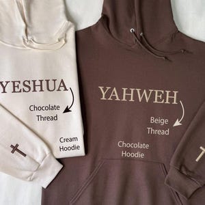 May include: Two hooded sweatshirts, one cream and one chocolate brown. The cream hoodie has "YESHUA" embroidered in chocolate thread, and a cross on the sleeve. The chocolate hoodie has "YAHWEH" embroidered in beige thread, and a cross on the sleeve.
