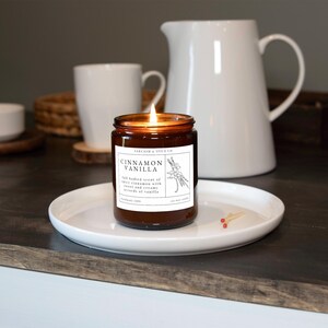 K&ouml;nnte beinhalten: Eine braune Glaskerze mit einem wei&szlig;en Etikett, auf dem "SARCASM & SPICE CO" und "CINNAMON VANILLA" steht. Das Etikett beschreibt den Duft auch als "vollmundiger Duft von w&uuml;rziger Zimt mit s&uuml;&szlig;en und cremigen Vanillenoten".