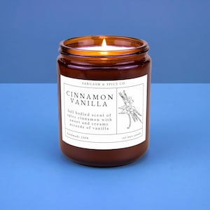 K&ouml;nnte beinhalten: Ein braunes Glasgef&auml;&szlig; mit einer Kerze und einem wei&szlig;en Etikett mit der Aufschrift "SARCASM & SPICE CO CINNAMON VANILLA full bodied scent of spicy cinnamon with sweet and creamy accords of vanilla handmade 100% soy wax candle".