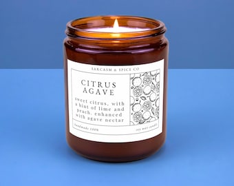 Könnte beinhalten: Ein braunes Glasgefäß mit einer Kerze und einem weißen Etikett, auf dem "SARCASM & SPICE CO CITRUS AGAVE" steht. Das Etikett beschreibt den Duft als "süße Zitrusfrüchte, mit einem Hauch von Limette und Pfirsich, verfeinert mit Agaven-Nektar". Das Etikett trägt außerdem die Aufschrift "handgefertigt 100% Sojawachskerze".