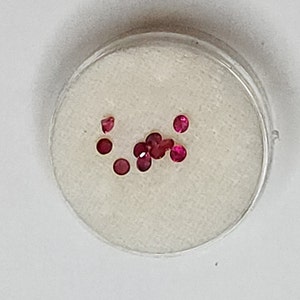 May include: A small white dish with a pile of small, round, pink gemstones.
