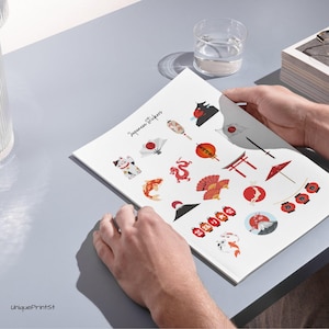 May include: A sheet of Japanese stickers with cultural motifs such as a lucky cat, koi carp, fans, and lanterns. The stickers are in red, white, and black, with the text "Japanese Stickers" at the top.