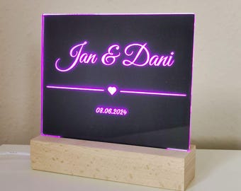 May include: A black acrylic sign with a wooden base. The sign has a pink neon inscription that reads "Jan & Dani" with a heart symbol and the date "08.06.2024".
