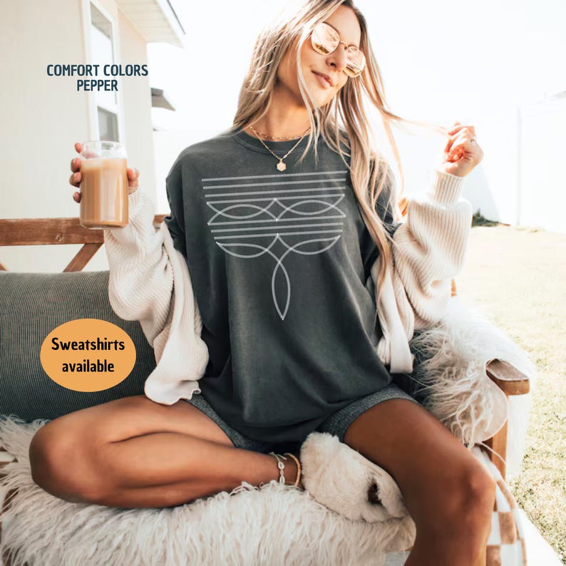 Peut inclure: Une femme portant un t-shirt surdimensionn&eacute; gris fonc&eacute; avec un motif g&eacute;om&eacute;trique blanc. Le t-shirt porte le texte "COMFORT COLORS PEPPER" en haut et "Sweatshirts available" en bas.
