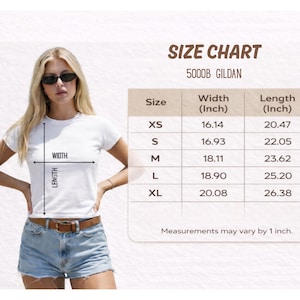 A woman wearing a white t-shirt and denim shorts, standing in front of a size chart for a 500DB GILDA t-shirt.