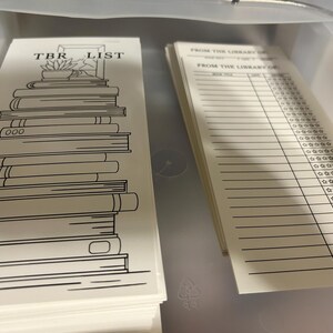 K&ouml;nnte beinhalten: Ein Stapel wei&szlig;er TBR-Listenkarten mit einer schwarzen Strichzeichnung von B&uuml;chern und dem Text "TBR LIST". Daneben ein Stapel linierter Karten mit dem Text "FROM THE LIBRARY OF" und Sternbewertungsabschnitten.