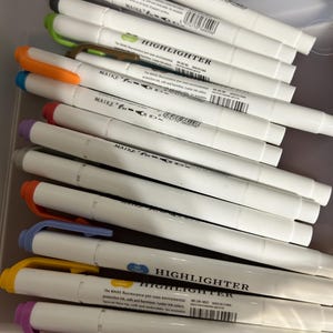 K&ouml;nnte beinhalten: Eine Ansammlung wei&szlig;er MAIKE Textmarker mit verschiedenfarbigen Kappen, darunter Gelb, Orange, Gr&uuml;n und Lila. Der Text "HIGHLIGHTER" ist auf der Seite der Stifte aufgedruckt. Die Stifte befinden sich in einem transparenten Beh&auml;lter.
