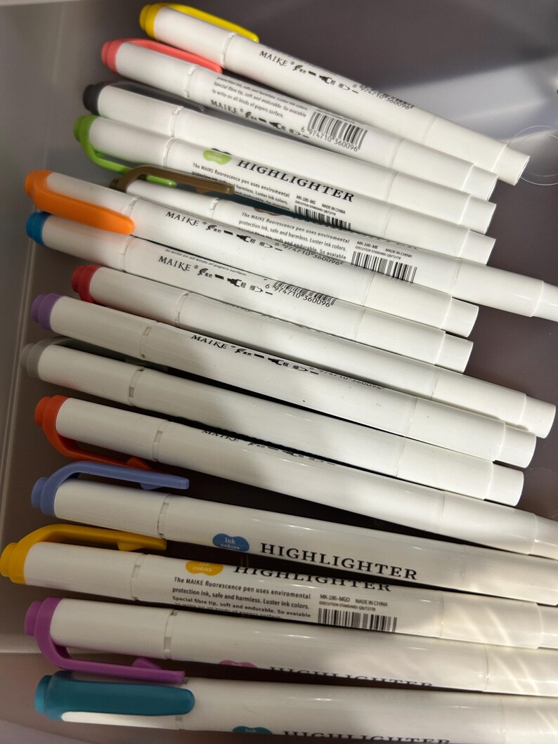 K&ouml;nnte beinhalten: Eine Ansammlung wei&szlig;er MAIKE Textmarker mit verschiedenfarbigen Kappen, darunter Gelb, Orange, Gr&uuml;n und Lila. Der Text "HIGHLIGHTER" ist auf der Seite der Stifte aufgedruckt. Die Stifte befinden sich in einem transparenten Beh&auml;lter.