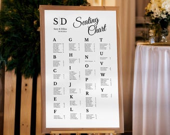 May include: A wooden framed seating chart with the text "SD Seating Chart" and the names of guests listed alphabetically. The chart is displayed on an easel, with a wooden background and greenery.