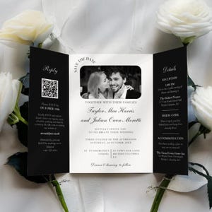 Peut inclure: Une invitation de mariage pliée en trois volets, en noir et blanc. Elle présente une photo d'un couple, les détails de l'événement et les informations de réponse. Des roses blanches sont en arrière-plan.