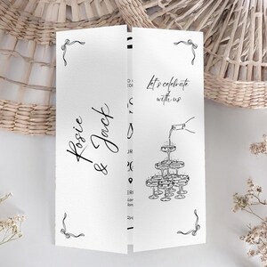 May include: A white wedding invitation card with black script that reads "Rosie & Jack" and "Let's celebrate with us." The card features a champagne tower illustration and decorative bow accents. The card is folded.