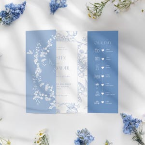 Könnte beinhalten: Eine hellblaue Hochzeitseinladungssuite mit floralen Illustrationen und Veranstaltungsdetails. Die Einladung zeigt die Namen "Sien und Alexander" und einen Zeitplan für "Unser Tag". Das Design umfasst einen floralen Rand und Ereignissymbole.