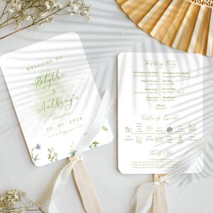 Puede incluir: Un abanico de programa de boda con fondo blanco e ilustraciones florales verdes. La parte delantera del abanico dice "Bienvenido a Blythe & Anthony's Wedding Day 10.07.2026" y la parte posterior del abanico enumera la fiesta de bodas y el orden de los eventos.