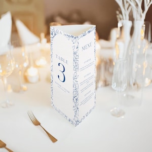 Może przedstawiać: Trójstronna karta menu na stół z kwiatowym wzorem w kolorze granatowym. Karta wyświetla "Stolik 3" oraz menu z opcjami przystawki, dania głównego i deseru. Na dole wydrukowane są nazwiska "Hannah & Tyler".