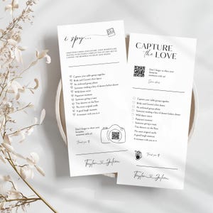 May include: Two white cards with black text. One card reads "i spy..." and the other reads "Capture the Love." Both cards have a list of prompts and a camera graphic with a QR code. The cards are for a wedding.